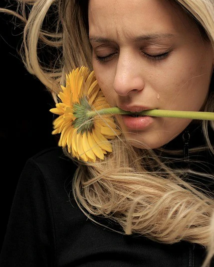 femme avec une larme sur la joue serrant une tige de fleur entre ses dents symbolisant la peine