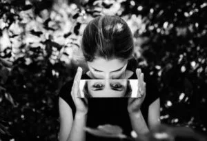 photo noir et blanc femme assise tenant un miroir pour voir le reflet de ses yeux
